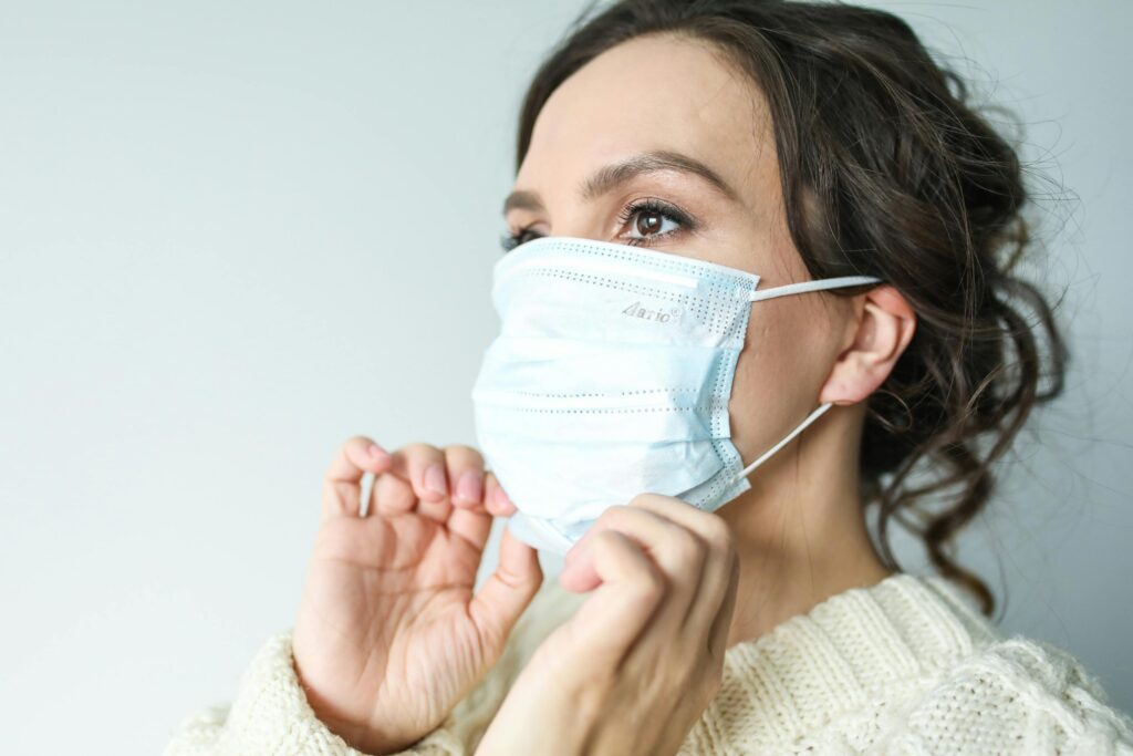 Adult woman adjusting blue surgical mask indoors for health safety.